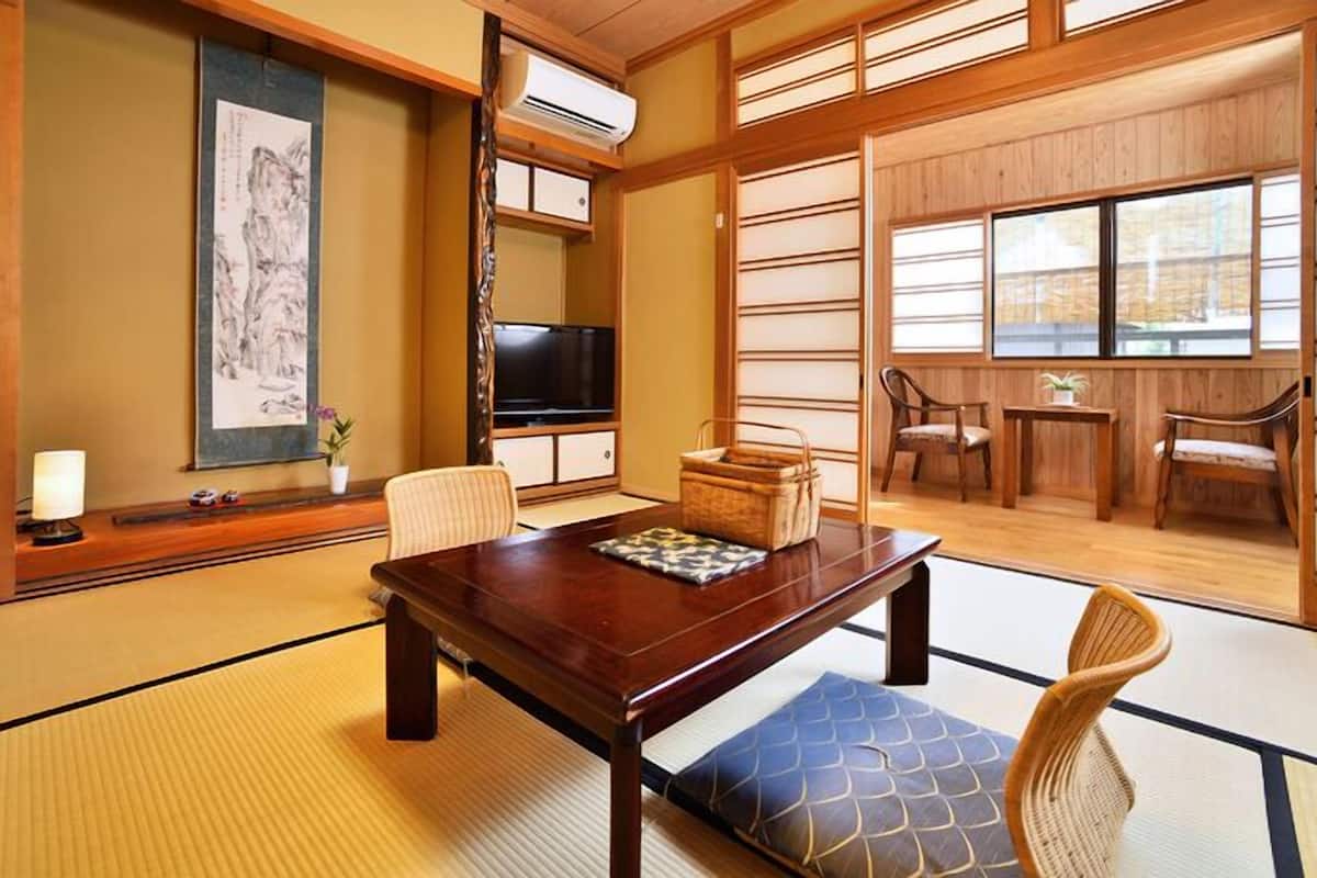 A traditional Japanese room with tatami flooring, a low table, chairs, a TV, and sliding doors.