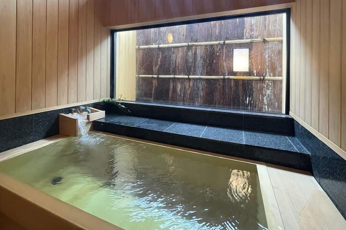 A hot spring bath with a wooden interior, a window with a bamboo blind, and a small plant on the windowsill.