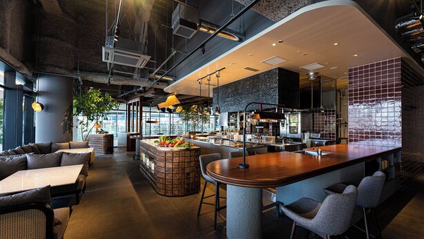 A modern restaurant with a bar area, seating, and a kitchen visible in the background. - Kawagoe Tobu Hotel (Kawagoe)