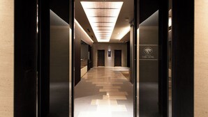 A modern hotel lobby with a long corridor, dark wooden doors, and a ceiling with a geometric light fixture. - Kawagoe Tobu Hotel (Kawagoe)