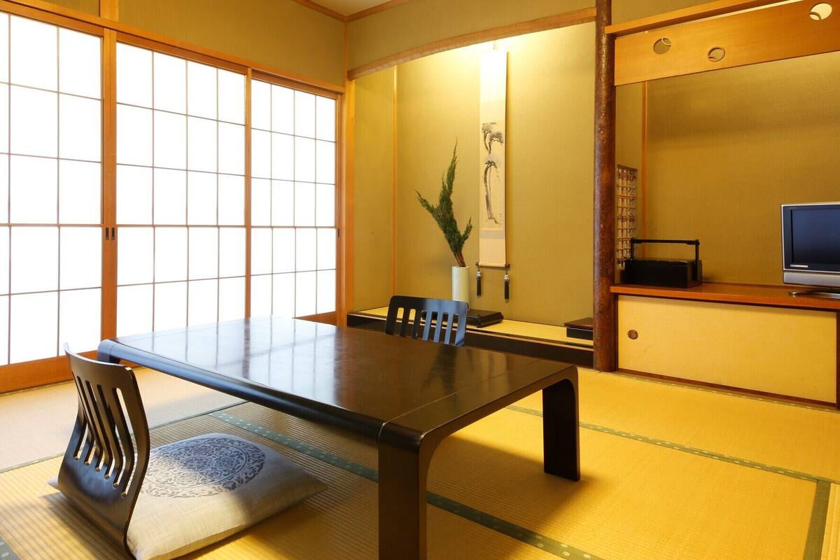 Una habitación japonesa tradicional con suelo de tatami, una mesa baja y un televisor sobre un mueble de madera.