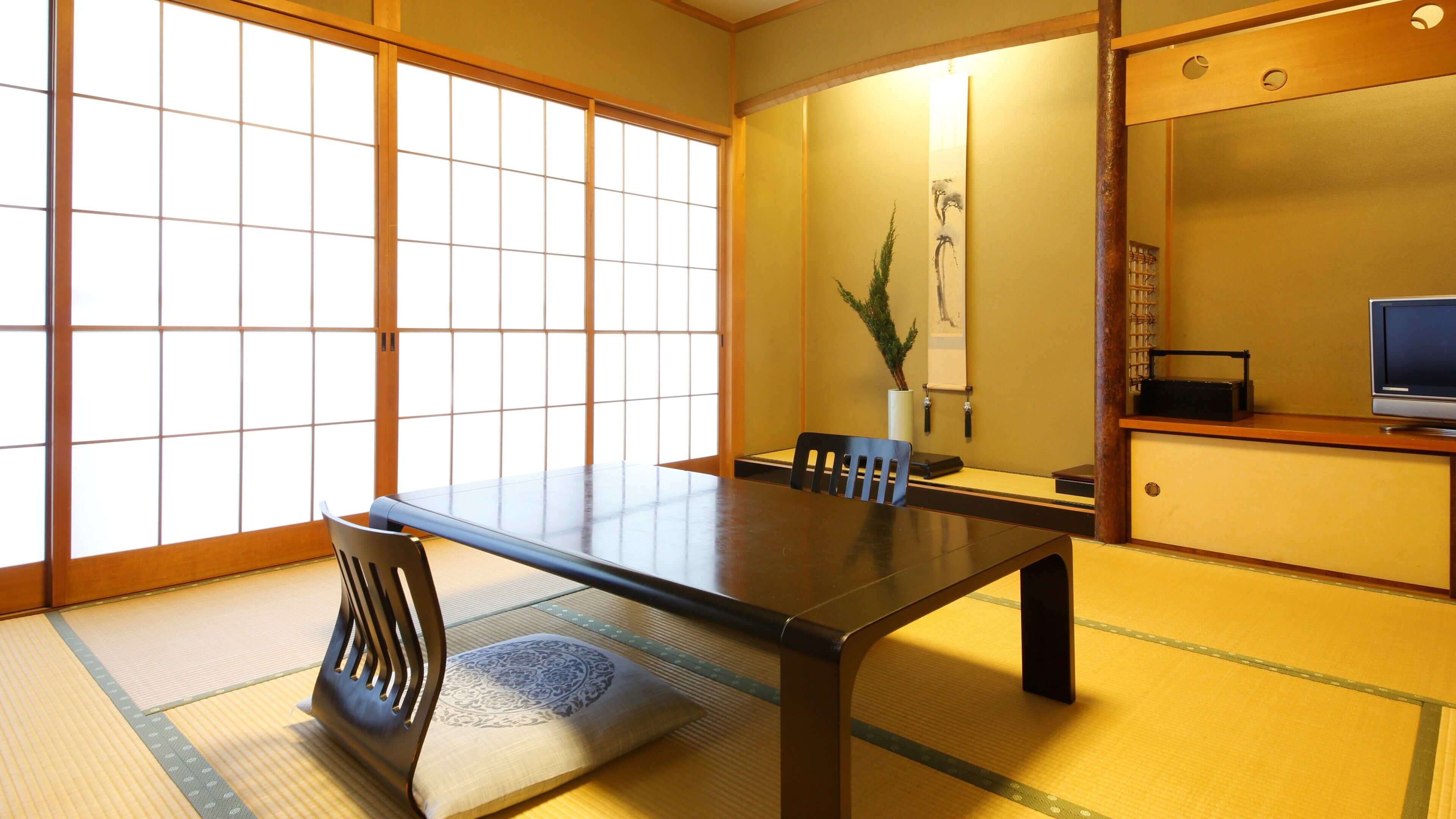 A traditional Japanese room with tatami flooring, a low table, and a television on a wooden cabinet.