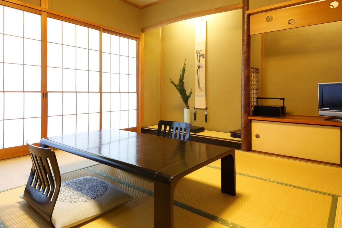 Una habitación japonesa tradicional con suelo de tatami, una mesa baja y un televisor sobre un mueble de madera.