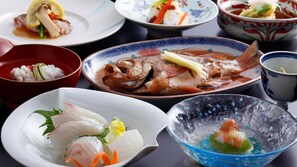 A variety of dishes on a table, including sashimi, a whole fish, and a bowl of rice.