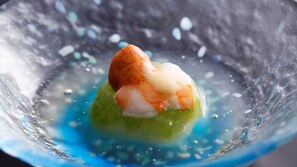 A dessert with a shrimp on top, served in a glass bowl with a blue liquid base.