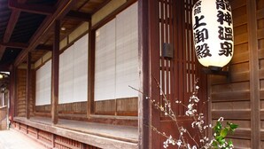 A traditional wooden building with sliding doors, a potted plant with white flowers, and a hanging sign with Japanese characters. - Kamigoten Ryokan (Tanabe)
