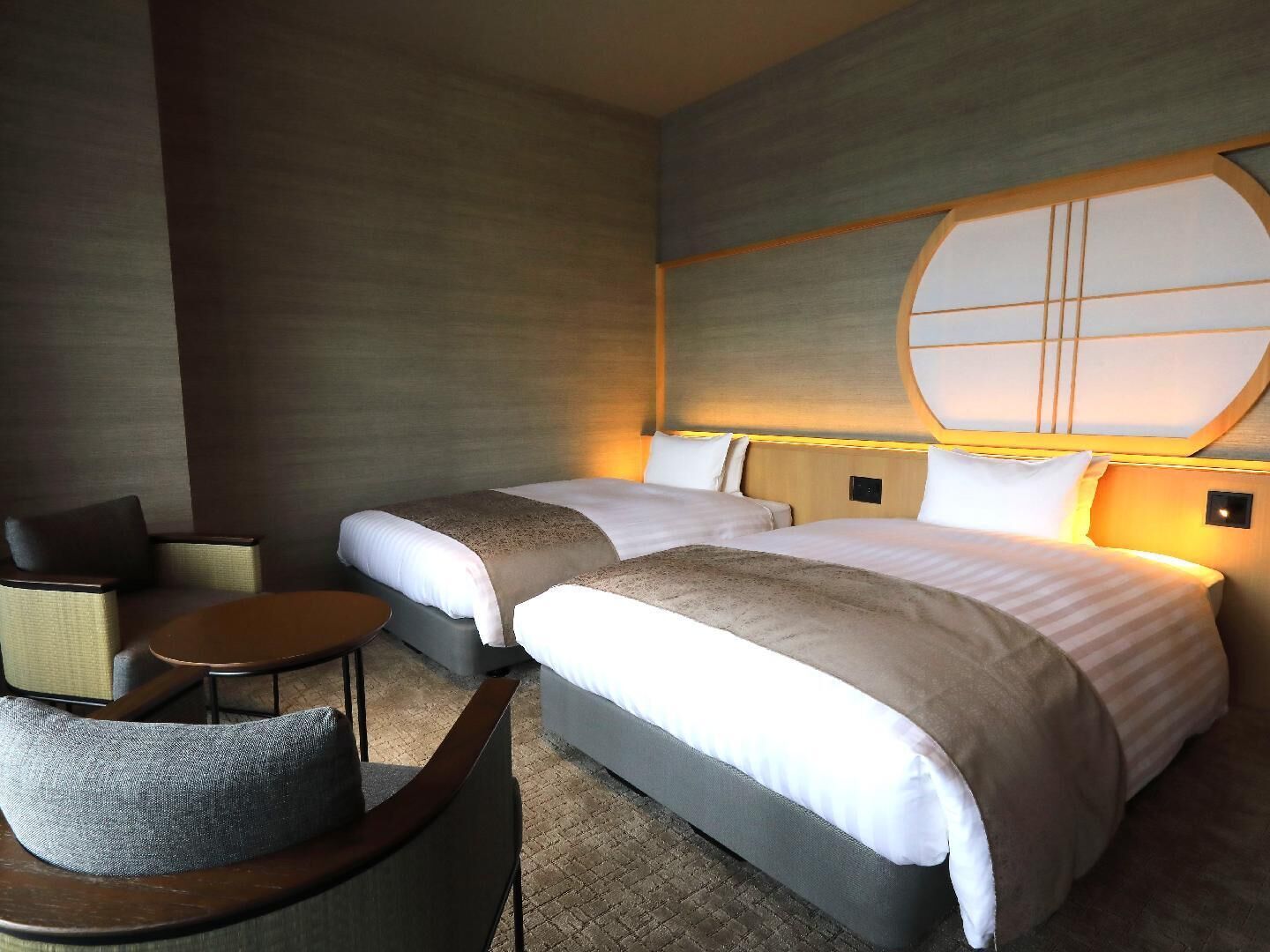 A hotel room with two beds, a small round table, and a chair.