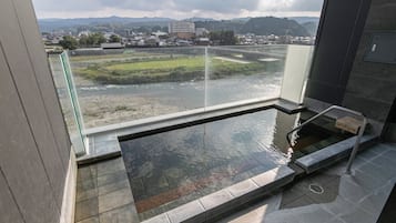A modern indoor pool with a glass railing, a view of a river and mountains, and a stone-tiled floor.