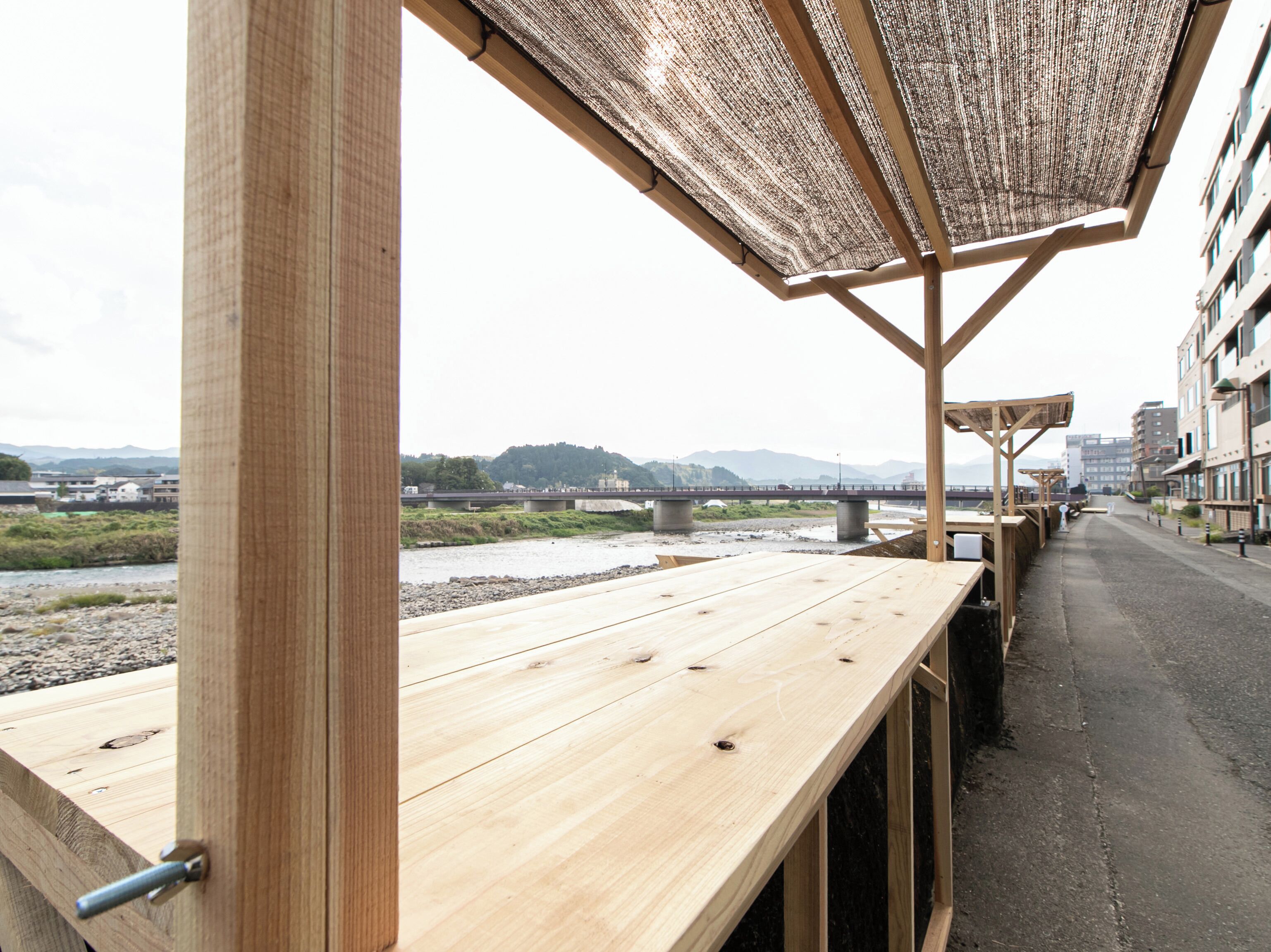 A wooden deck with a view of a river and a bridge, overlooking a cityscape with buildings and hills.