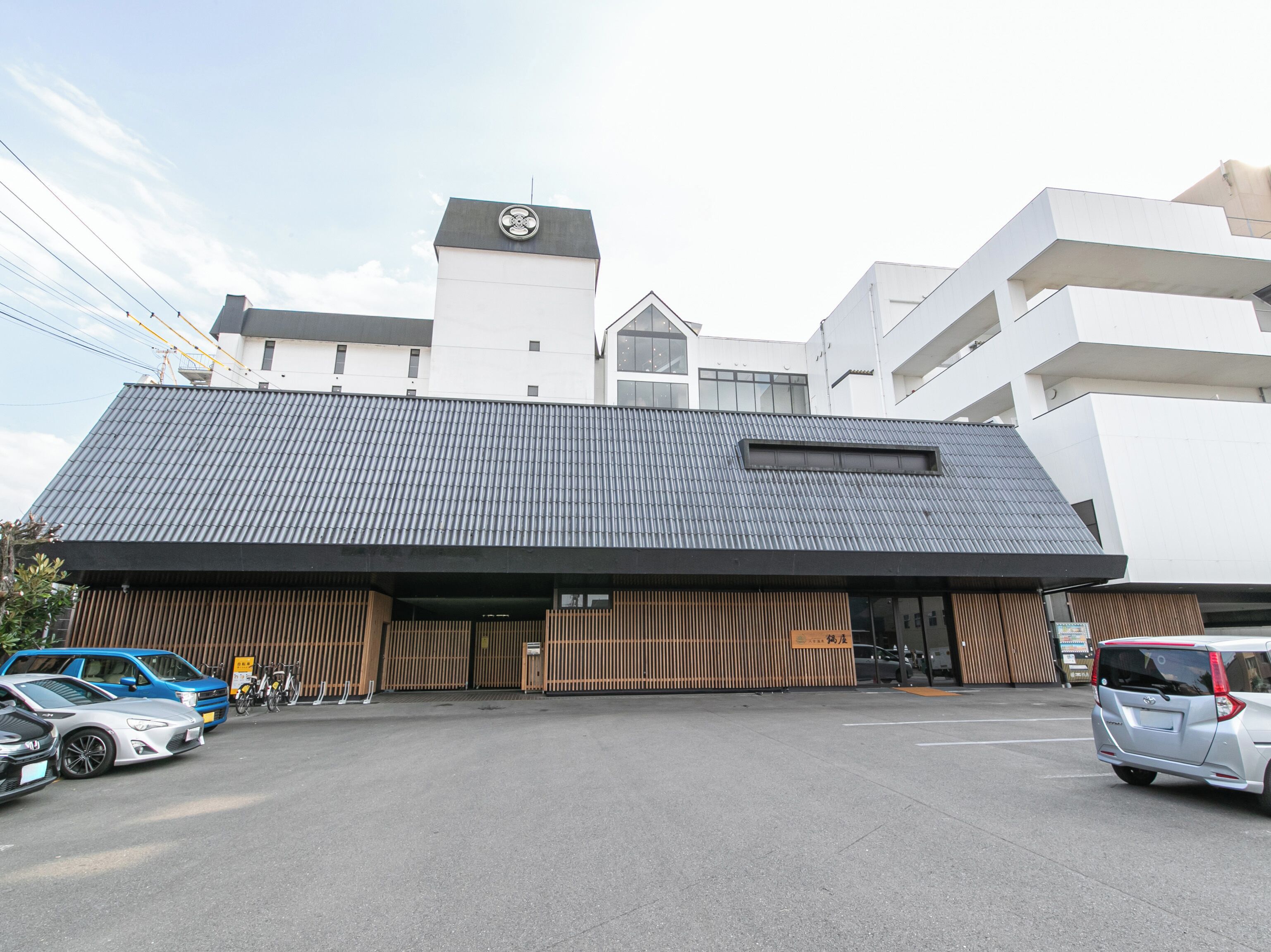 A modern building with a sloped roof and a large entrance. There are cars parked in front, and a bicycle is visible near the entrance.