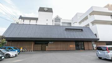 A modern building with a sloped roof and a large entrance. There are cars parked in front, and a bicycle is visible near the entrance.