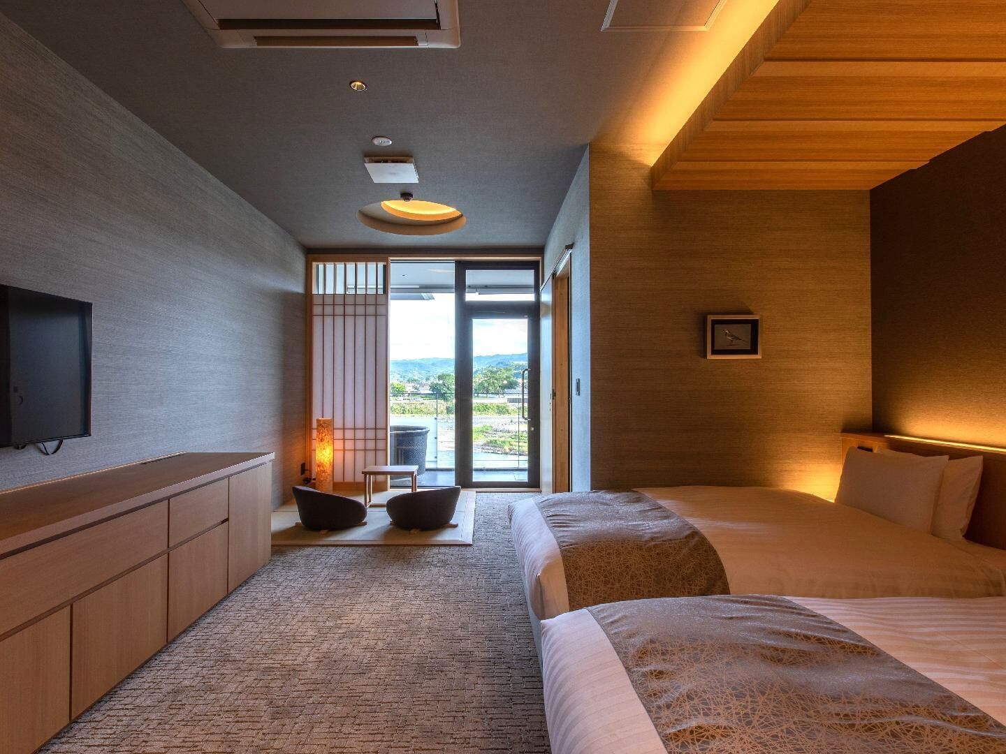 A modern hotel room with a large bed, a TV, a seating area with a view, and a wooden ceiling.