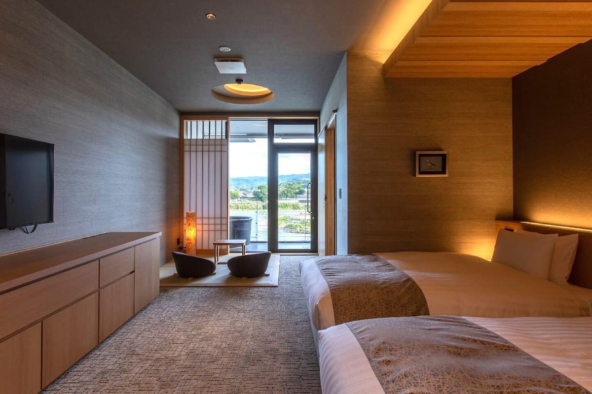 A modern hotel room with a large bed, a TV, a seating area with a view, and a wooden ceiling.