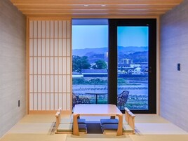 Una habitación japonesa tradicional con suelo de tatami, una mesa baja y un puertas correderas que dan a un barrio residencial.