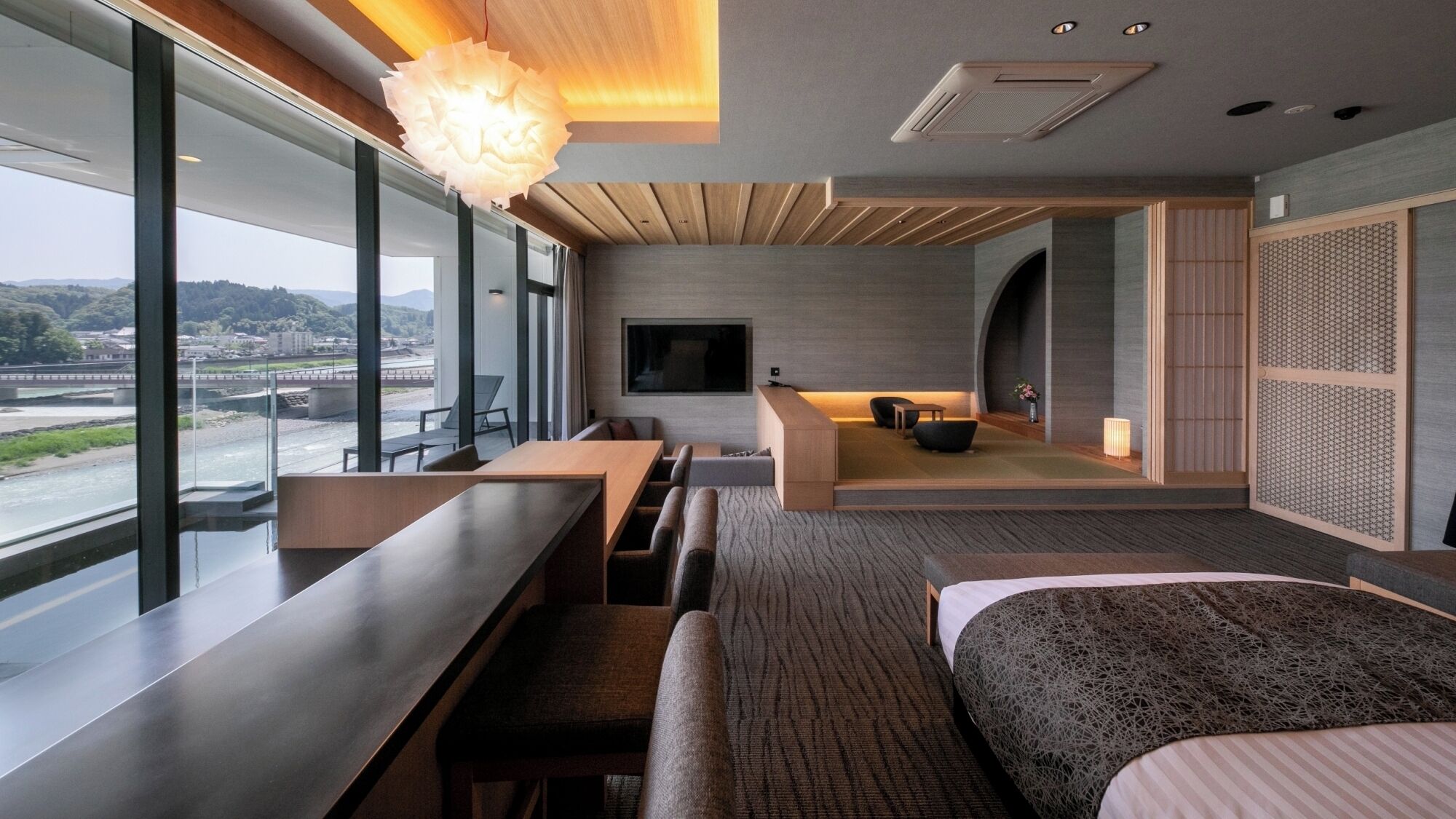 A modern hotel room with a large window, a sofa, a bed, and a TV.
