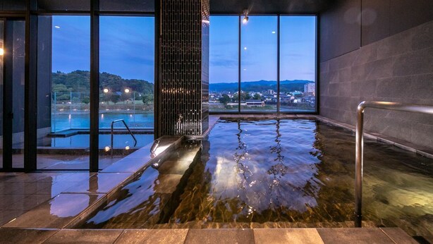 A modern indoor pool with clear glass walls, a water feature, and a view of the surrounding landscape. - Hitoyoshi Onsen Nabeya (Hitoyoshi)