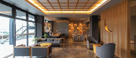 A modern lobby with a high ceiling, seating area, and a bar.