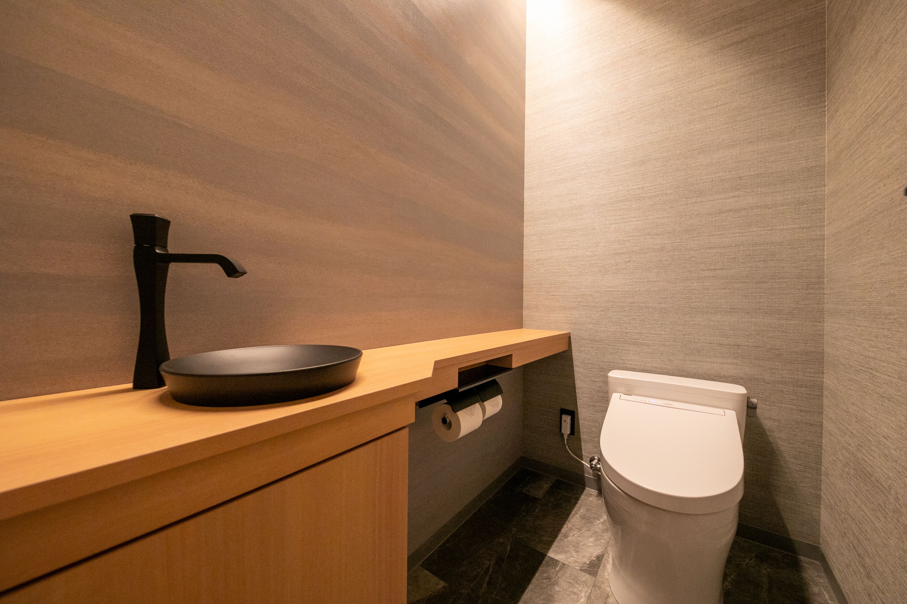 Un baño moderno con tocador de madera, lavamanos negro y retrete blanco.