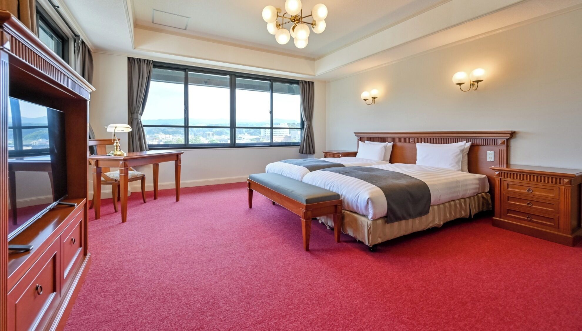 A hotel room with a large bed, a desk, a TV, and a view of the city through the window.