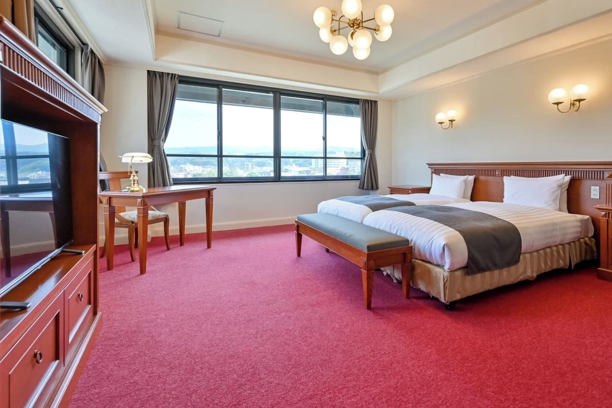 Une chambre d’hôtel avec un grand lit, un bureau, une télévision et une vue sur la ville par la fenêtre.