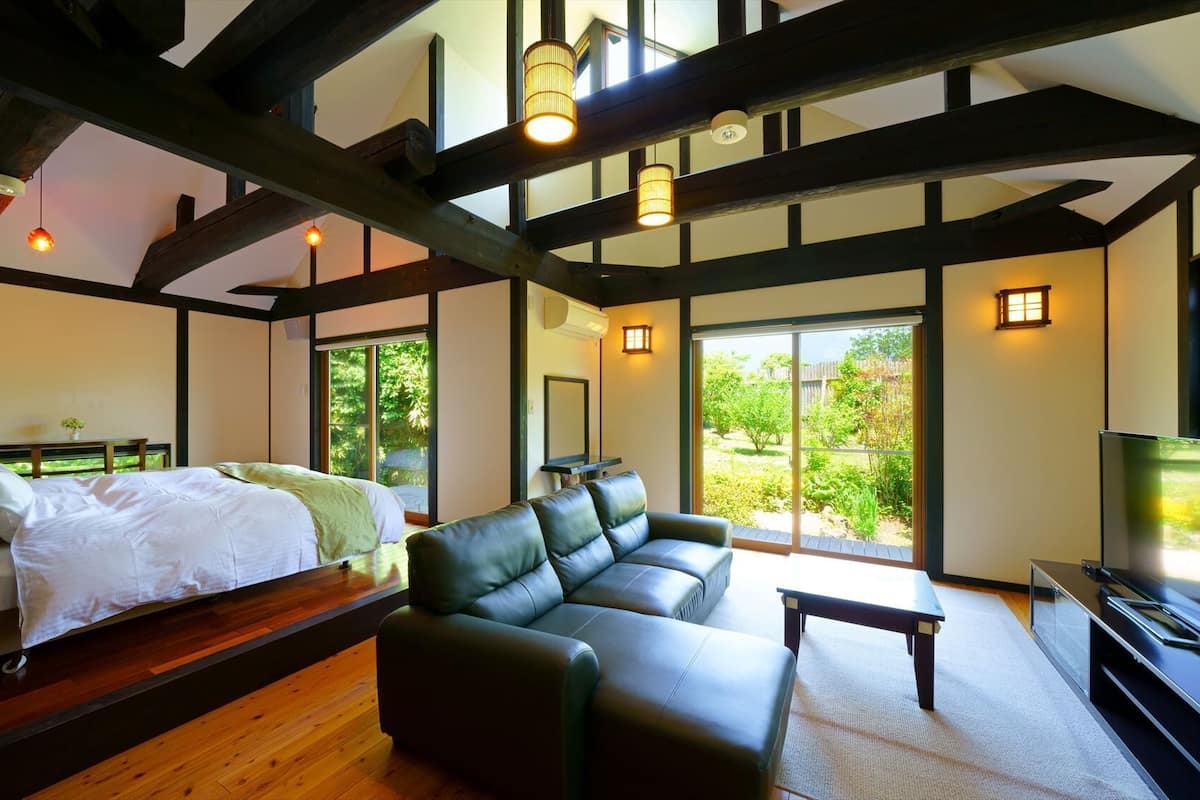 Una habitación con cama, sofá, televisor y ventanas amplias.