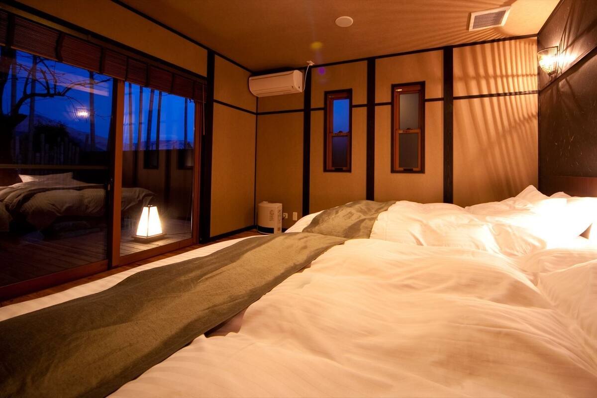 A hotel room with a bed, a nightstand, a lamp, a window with a view, and a sliding door.