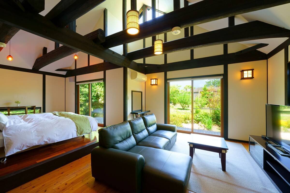 A room with a bed, a sofa, a TV, and large windows.