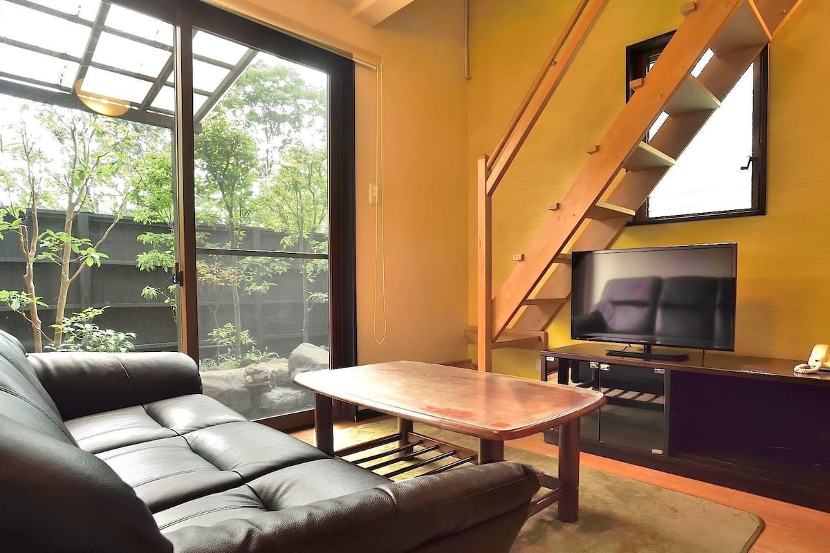 A modern living room with a sofa, a coffee table, a TV, and a staircase.