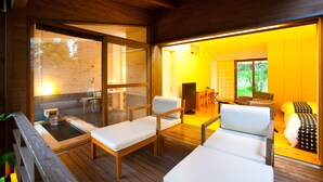 Un interior de madera con un jacuzzi, dos sillones de descanso y una cama con ropa de cama estampada.