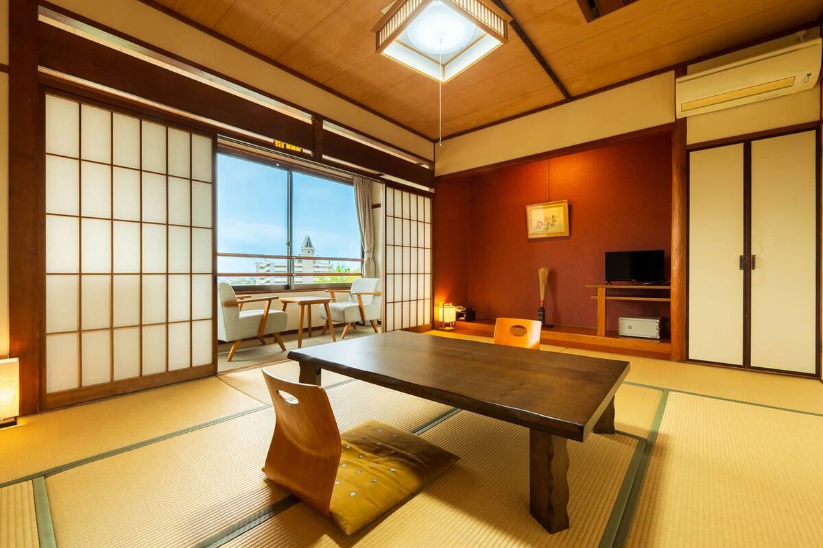 Ett traditionellt japanskt rum med tatamimattor på golvet, ett lågt bord, skjutdörrar och utsikt över omgivningen.