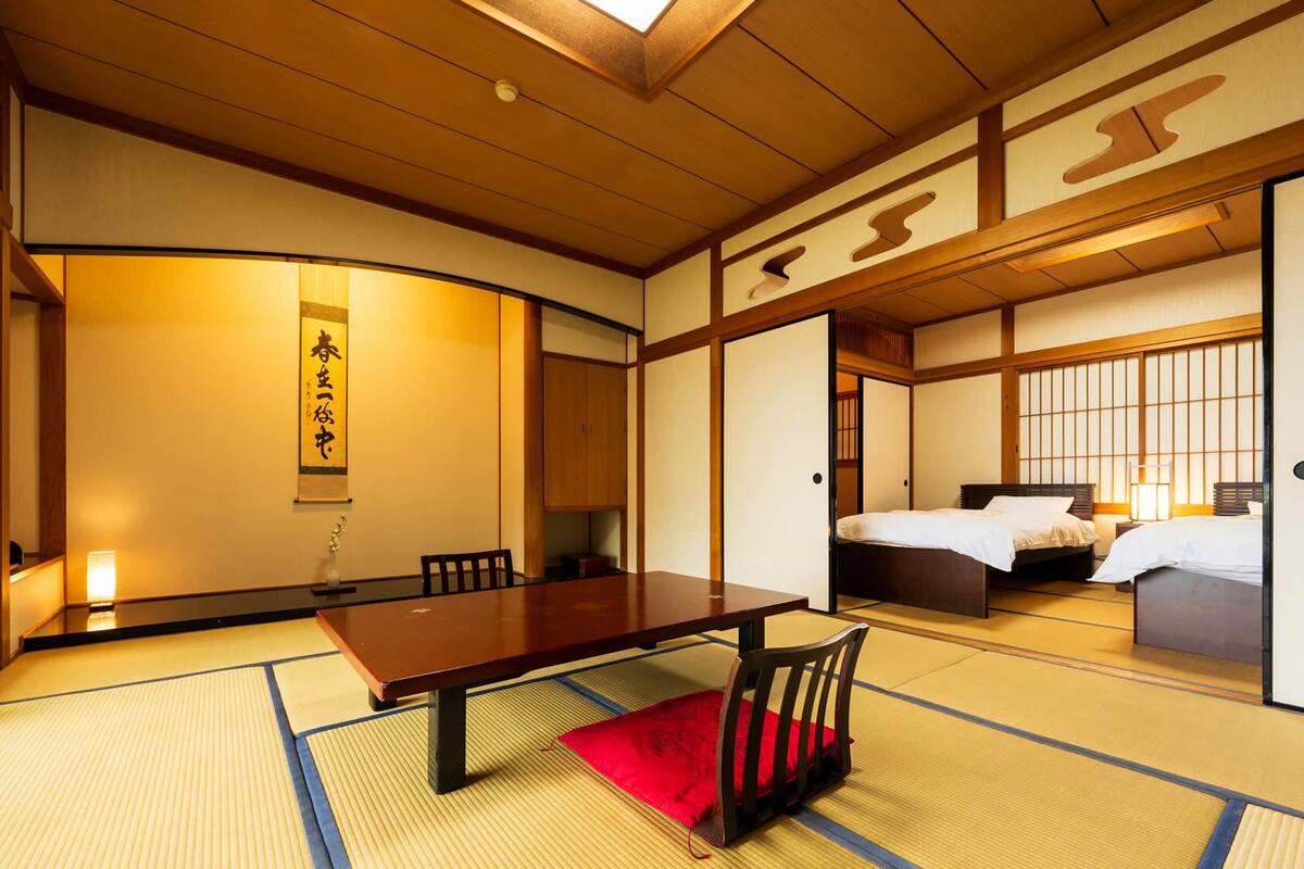 Ett traditionellt japanskt rum med tatamimattor på golvet, ett träbord, en säng och skjutdörrar.