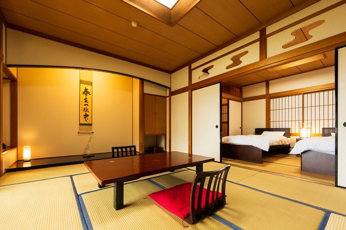 A traditional Japanese room with tatami flooring, a low wooden table, a bed with white bedding, and sliding doors.