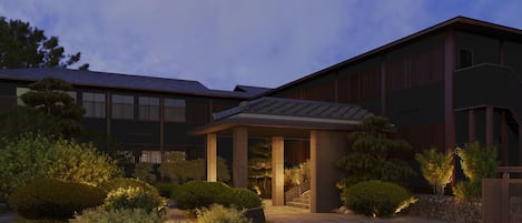 A modern building with a covered entrance, surrounded by well-maintained landscaping and trees.