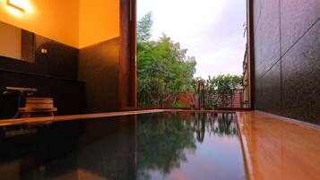 Un baño moderno con piso reflectante, un banco de madera y vistas a un jardín a través de una puerta de vidrio.