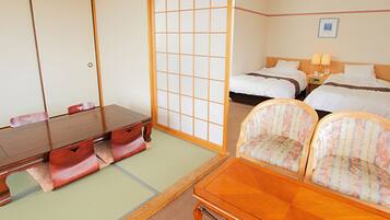 A traditional Japanese room with tatami flooring, a low wooden table, two tatami mats for seating, a bed with white bedding, and a nightstand with lamps.