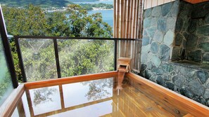 A balcony with a stone wall, wooden floor, and a view of a coastal landscape. - Hotel Manyomisaki (Aioi)