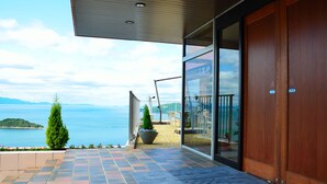A hotel entrance with a glass door, a view of the sea, and a tiled patio area. - Hotel Manyomisaki (Aioi)