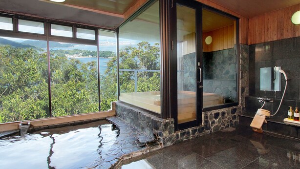 A modern bathroom with a stone-tiled floor, a glass-enclosed shower, and a view of a lush landscape. - Hotel Manyomisaki (Aioi)