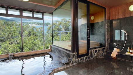 A modern bathroom with a stone-tiled floor, a glass-enclosed shower, and a view of a lush landscape.. Hotel Manyomisaki
