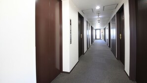 A long, narrow hallway with doors on both sides, carpeted floor, and a ceiling with recessed lighting. - Urban Hotel Tokyo Fuchu Nisiguchi (Fuchu)