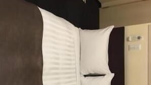 A corner of a hotel room with a bed, a nightstand, and a door. - Urban Hotel Tokyo Fuchu Nisiguchi (Fuchu)
