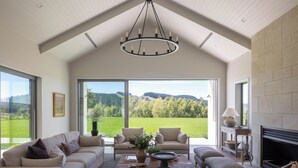 A spacious living room with a high ceiling, large windows, and a fireplace. - Craggy Range Luxury Vineyard Retreat (Tuki Tuki)