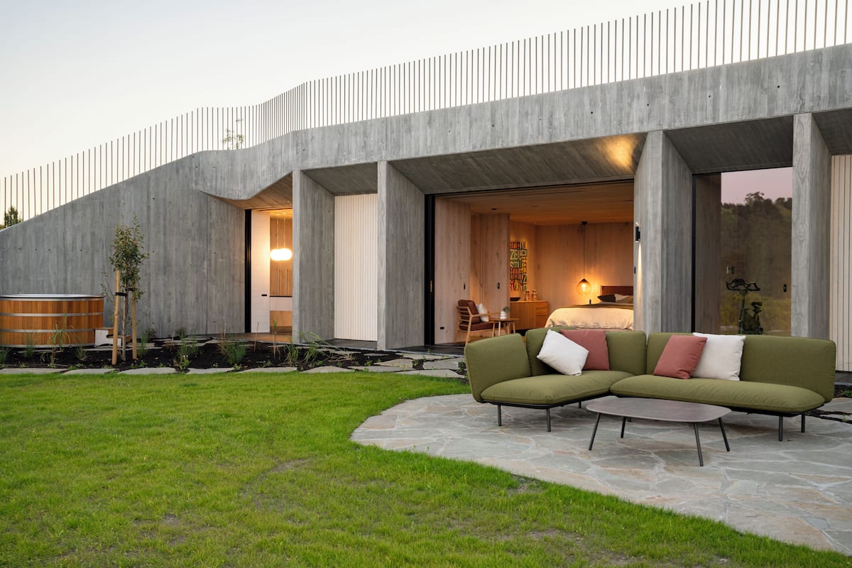 A modern house with a large outdoor seating area, a stone patio, and a large window overlooking the garden.