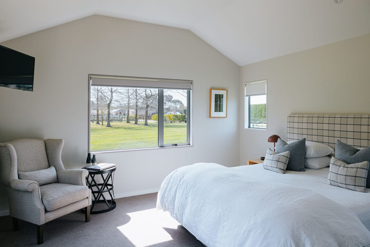 A bedroom with a large window, a bed with pillows, a chair, and a small table.