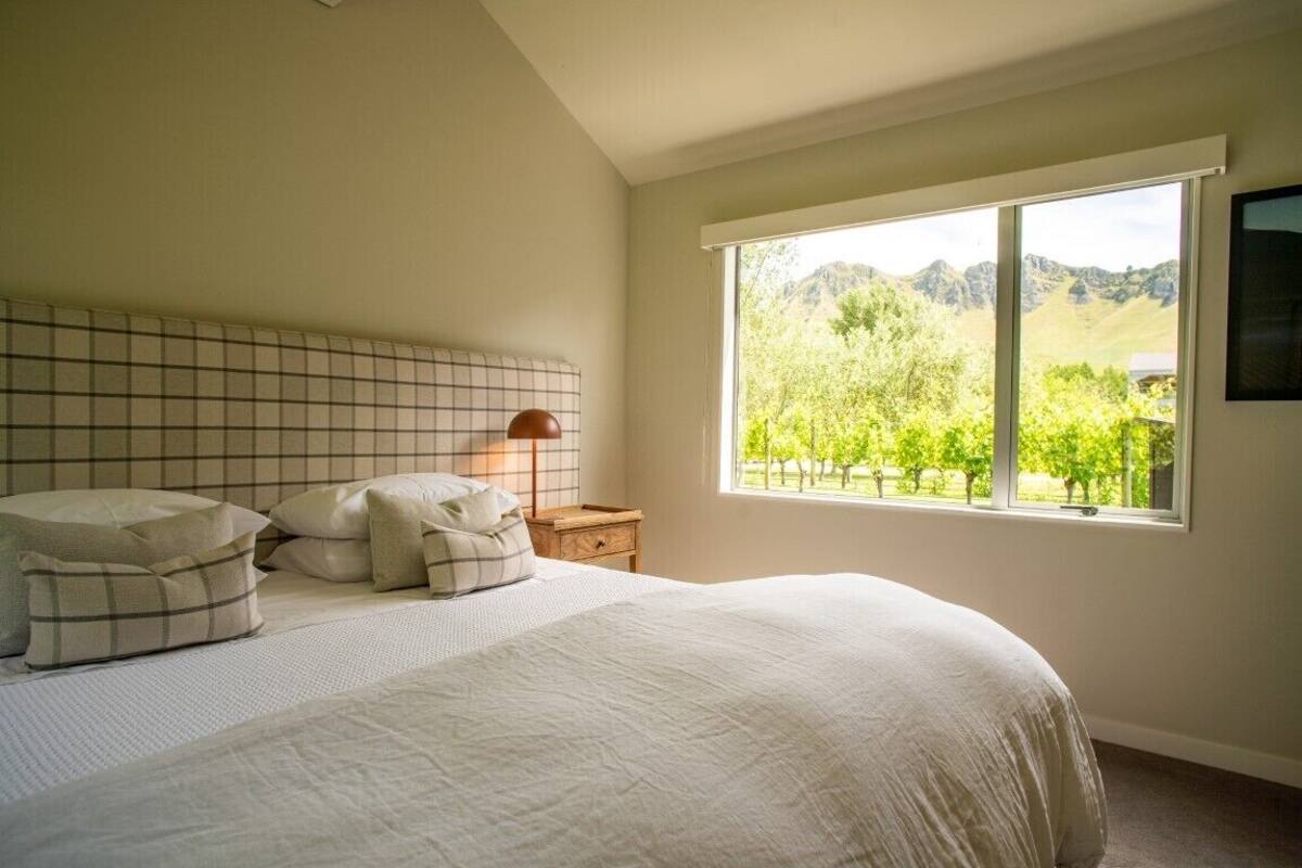 A bedroom with a large bed, a nightstand, a lamp, and a window with a view of trees and mountains.