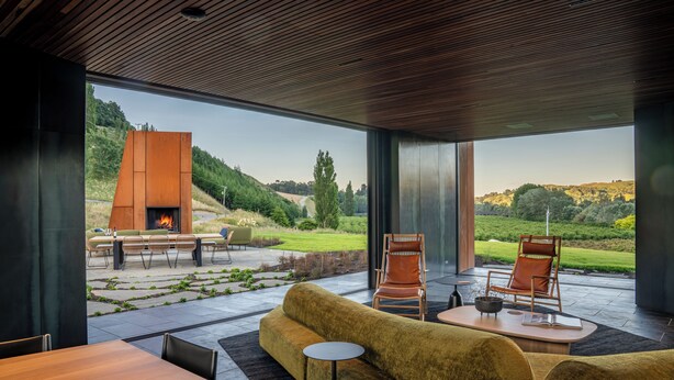 A modern interior with a large window, a sofa, two chairs, a table, and a fireplace. - Craggy Range Luxury Vineyard Retreat (Tuki Tuki)