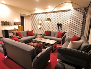 Una sala de estar moderna con sofás grises, cojines rojos, una mesa de centro y un papel tapiz estampado.