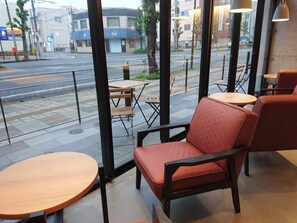 A café with red cushioned chairs and wooden tables, large windows with a view of the street. - Green Rich Hotel Kurume (Kurume)