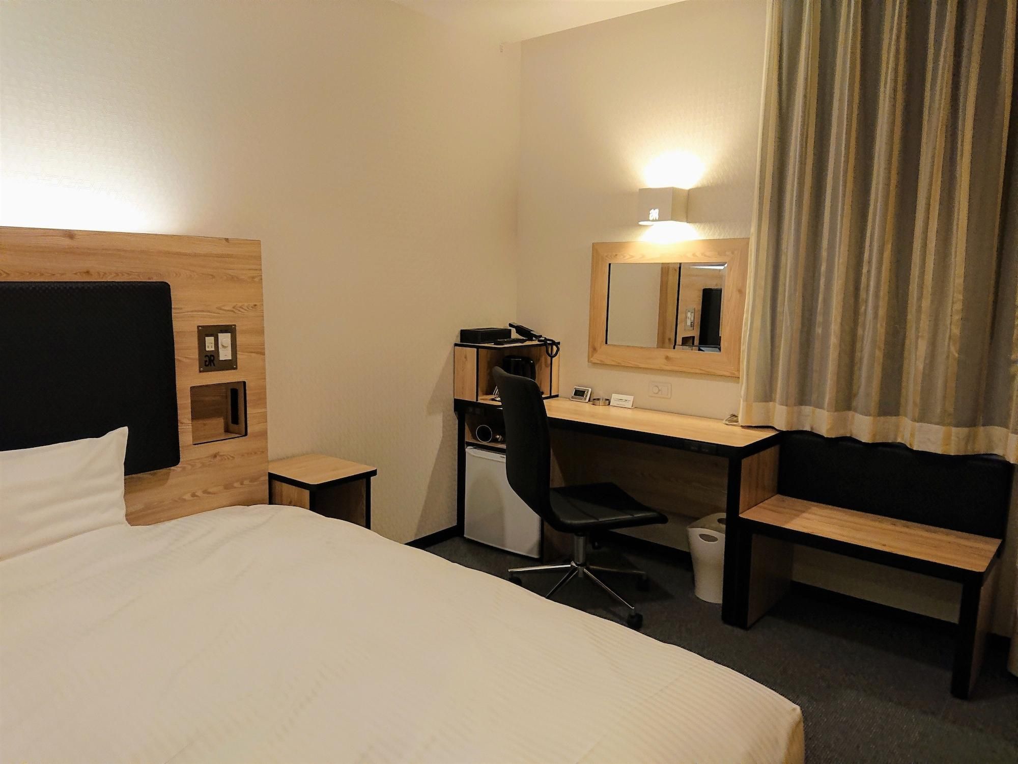 Une chambre d’hôtel avec un lit, un bureau, une chaise, un miroir et un rideau.