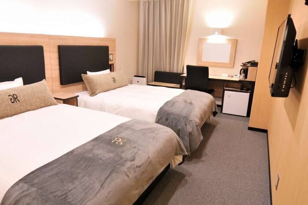 A hotel room with two beds, a desk, a television, and a small refrigerator.